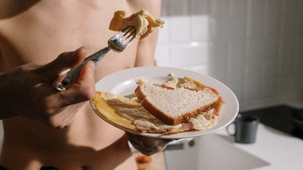 Man standing in kitchen, eating omelette with toast. Morning meal indoors.